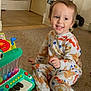 Jayden is registered to the contest to win money with this photo: child, toddler, smiling, pajamas, toy_piano, playroom, carpet, indoor, sitting, happy, face, toy, dump_truck, steering_wheel, pet, dog, colorful, music_toy, early_childhood, floor