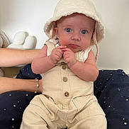 Ezio participe au concours pour gagner de l'argent avec cette photo : baby, infant, hat, beige_clothing, sitting, blue_eyes, hands, cushion, star_pattern, arm, bracelet, indoor, portrait, cute, child, soft_lighting, face, person, young, home