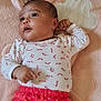 baby, infant, blanket, plush_toys, red_pants, white_shirt, patterned_clothing, heart_shape, cloud_shape, soft_texture, indoor, child, cute, lying_down, looking_up, curious, cozy, pink, white, red