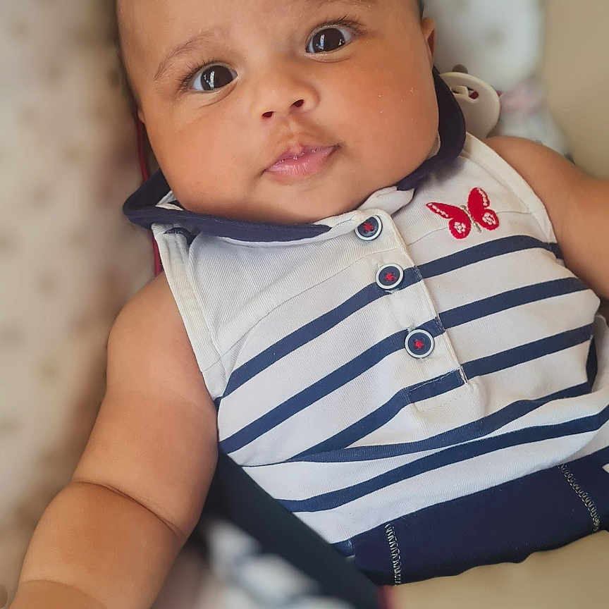 Cassy participe au concours pour gagner de l'argent avec cette photo : arm, baby, butterfly_patch, child, closeup, clothing, cushion, cute, eyes, face, hand, indoors, infant, lying_down, person, portrait, skin, smiling, soft_background, striped_outfit