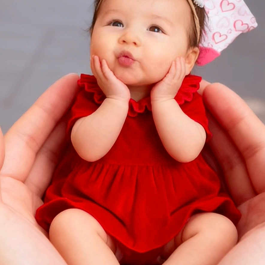 Jannah a rejoint le concours — aidez-le/la à gagner de superbes lots ! baby, child, red_dress, hands, cute, portrait, headband, face, infant, skin, smile, pose, background_blur, holding, small_feet, adorable, expression, lock_screen, phone_ui, indoor
