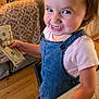 toddler, child, money, cash, smile, denim_overalls, pink_shirt, indoor, kitchen_counter, wood_floor, plant, television, furniture, happy, portrait, hand, face, person, home, cute
