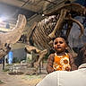 Melia Bloom joined the competition — help win amazing prizes! child, toddler, baby, museum, dinosaur_skeleton, fossil, exhibit, orange_dress, sun_pattern, portrait, indoor, education, natural_history, skeleton, large_animal, parent, shoulder, standing, serious_expression, photography
