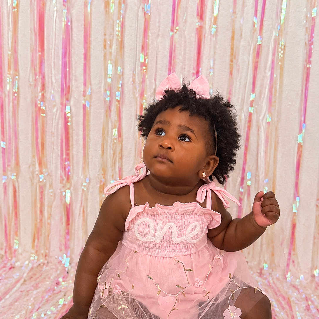 Melia Bloom joined the competition — help win amazing prizes! baby, child, portrait, sitting, pink_dress, bow, curly_hair, smiling, looking_up, earrings, sparkly_background, party, celebration, indoor, studio, fashion, tulle_skirt, floral_details, dark_skin, photography