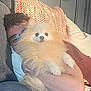 arm, blanket, casual, comfort, couch, curly_hair, dog, fluffy, furniture, glasses, home, indoor, lamp, living_room, person, pet, pomeranian, relaxing, resting, smiling