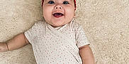 Livia participe au concours pour gagner de l'argent avec cette photo : baby, infant, smile, headband, red_clothing, shorts, lying_down, carpet, happy, cute, child, portrait, indoor, skin, face, hand, playful, young, apparel, one_person