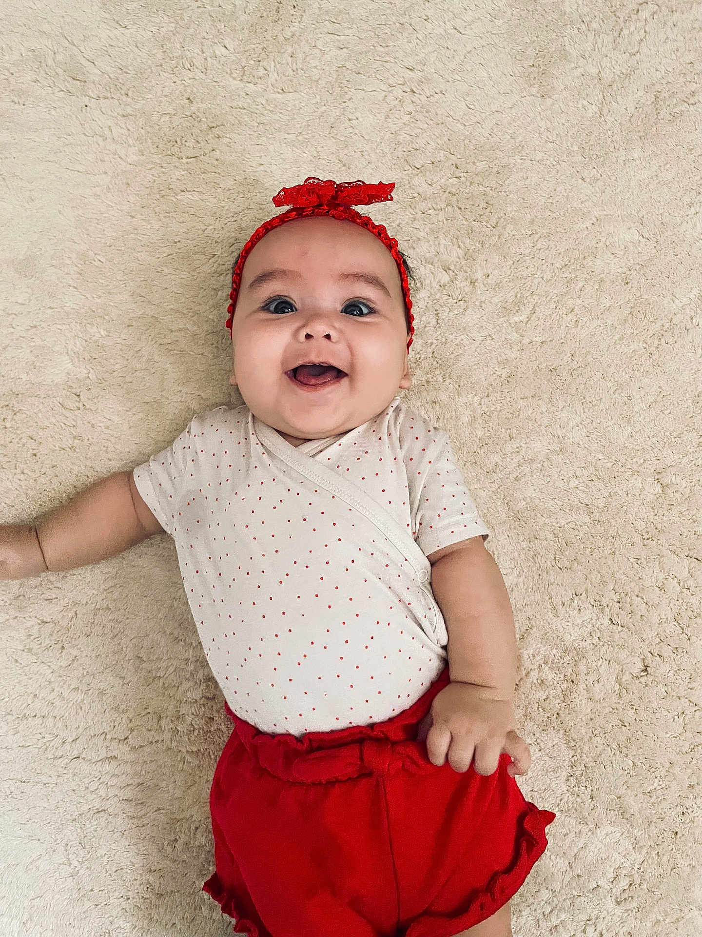 Livia participe au concours pour gagner de l'argent avec cette photo : baby, infant, smile, headband, red_clothing, shorts, lying_down, carpet, happy, cute, child, portrait, indoor, skin, face, hand, playful, young, apparel, one_person