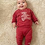 baby, infant, red_clothing, teddy_bear_patch, lying_down, carpet, tongue_out, cute, child, smiling, happy, cozy, sock, playful, portrait, indoors, soft_texture, head, face, person