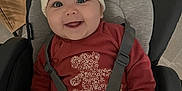 Livia a rejoint le concours — aidez-le/la à gagner de superbes lots ! baby, car_seat, child, cozy, cute, face, happy, harness, hat, indoor, infant, knit_hat, person, plush_design, pom_poms, red_clothing, seat, sitting, smile, toddler