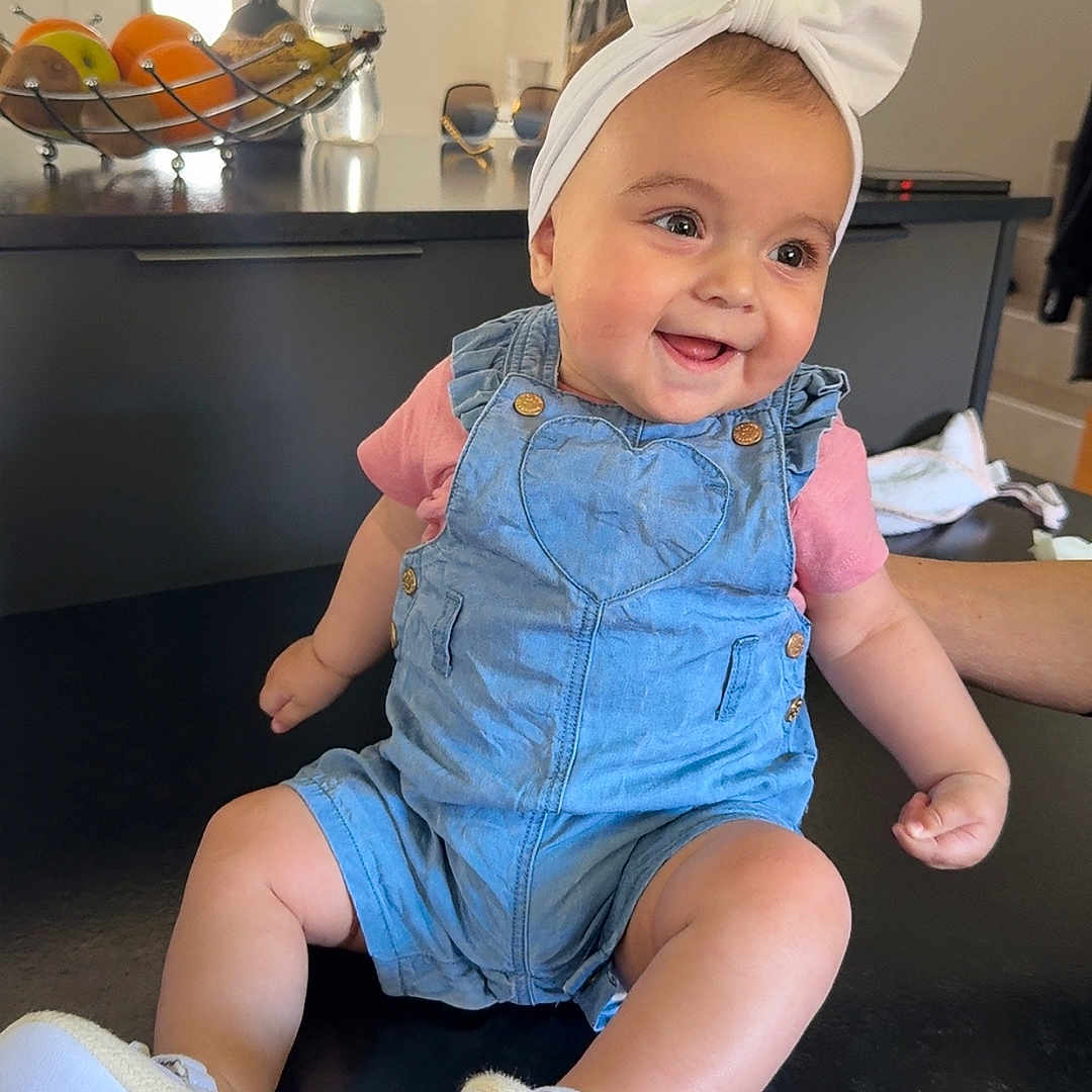 Kataleya a rejoint le concours — aidez-le/la à gagner de superbes lots ! baby, banana, bow, child, counter, cute, denim, footwear, fruit_basket, happy, headband, home_decor, indoor, kitchen, orange, person, portrait, romper, shoe, smiling