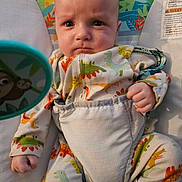 Josiah is registered to the contest to win money with this photo: baby, infant, dinosaur_pajamas, baby_seat, child, cute, serious_expression, clothing, indoor, person, face, portrait, fist, straps, patterned_clothing, toy, colorful, young_child, seated, baby_bouncer