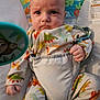 baby, infant, dinosaur_pajamas, baby_seat, child, cute, serious_expression, clothing, indoor, person, face, portrait, fist, straps, patterned_clothing, toy, colorful, young_child, seated, baby_bouncer