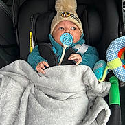 Izem a rejoint le concours — aidez-le/la à gagner de superbes lots ! baby, car_seat, blanket, pacifier, hat, pom_pom, knitwear, child, infant, toy, seatbelt, clothing, hand, face, indoor, car_interior, warm, cute, comfort, portrait