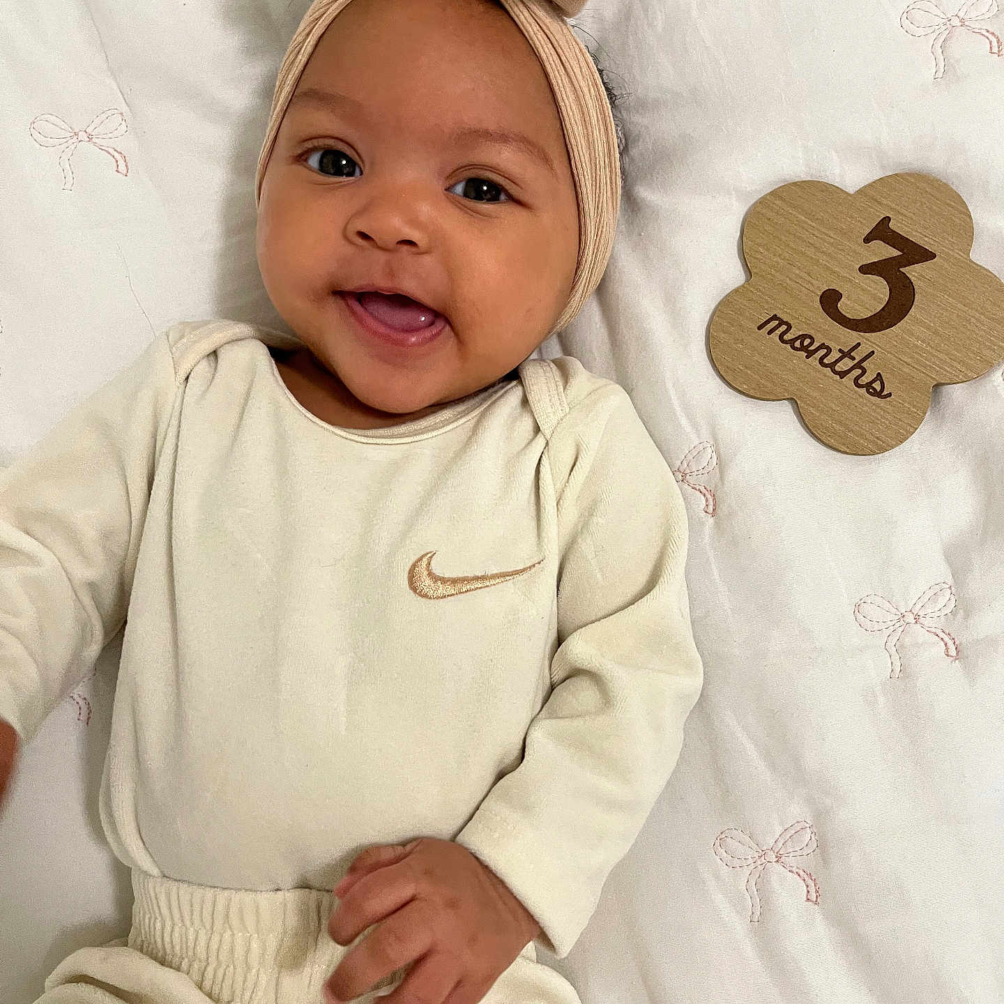 Zaniyah is registered to the contest to win money with this photo: baby, infant, smiling, headband, bow, beige_clothing, onesie, wooden_sign, 3_months, blanket, pink_bows, lying_down, cute, happy, portrait, closeup, child, person, indoors, soft_lighting