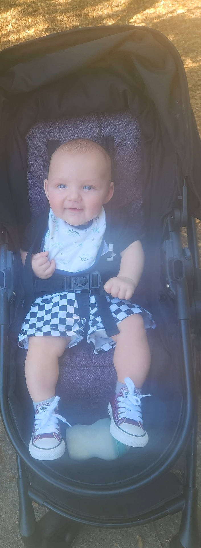Kai joined the competition — help win amazing prizes! baby, bib, bottle, casual_wear, checkered_shorts, child, cute, daylight, face, footwear, happy, infant, legs, outdoor, person, seatbelt, smiling, sneakers, stroller, summer