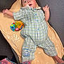 baby, infant, plaid_onesie, toy, changing_mat, floor, carpet, colorful_toy, patterned_clothing, child, indoor, cute, lying_down, expression, blue_eyes, short_hair, foot, hand, fabric, comfort