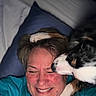 Cookie is registered to the contest to win money with this photo: affection, animal, bed, blue_shirt, close_up, cuddle, dog, face, fur, happy, head, human, indoor, laughing, paw, person, pet, pillow, playful, smile