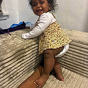 Cynthia joined the competition — help win amazing prizes! baby, child, smile, happy, curly_hair, leopard_print, dress, diaper, couch, tattoo, arm, hand, indoor, furniture, foot, skin, person, infant, climbing, playful
