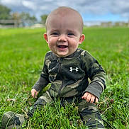 Weston joined the competition — help win amazing prizes! baby, child, smiling, grass, outdoor, camouflage_clothing, onesie, nature, sky, clouds, green, happy, sitting, infant, person, cute, portrait, young, bright, daytime