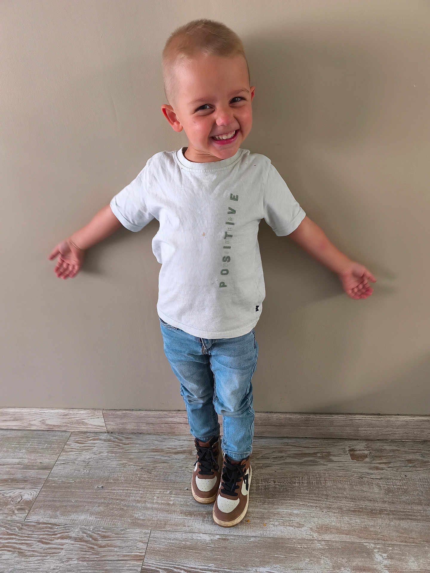 Owen a rejoint le concours — aidez-le/la à gagner de superbes lots ! child, boy, smiling, white_tshirt, jeans, sneakers, standing, indoor, wooden_floor, beige_wall, happy, casual_clothing, portrait, cute, short_hair, fashion, positive_message, person, full_body, playful