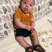 Yea Alexander is registered to the contest to win money with this photo: baby, infant, toddler, sitting, striped_shirt, mustard_shirt, navy_shorts, brown_sandals, shoes, patterned_pillow, bedding, blanket, cute, curious_expression, tongue_out, chubby_legs, indoors, portrait, nursery_blanket, adorable