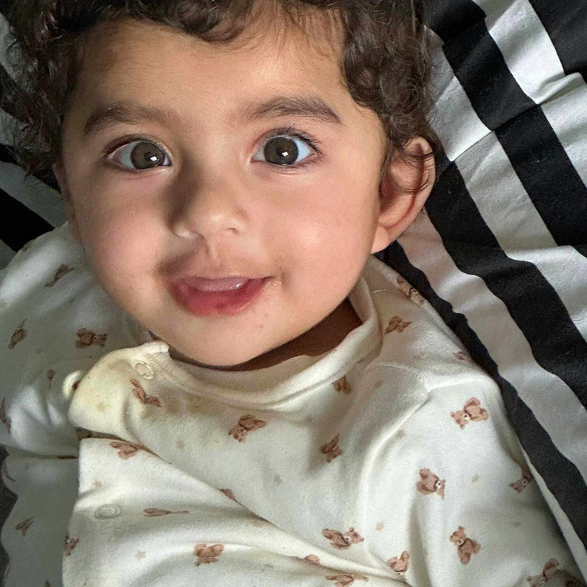 Sophia is registered to the contest to win money with this photo: baby, baby_clothes, blanket, child, clothing, curly_hair, cute, eyes, face, happy, indoors, infant, onesie, person, portrait, smile, striped_blanket, teddy_bear_pattern, toddler, young_child