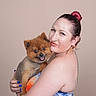animal, blue_nails, closeup, cute, dog, earrings, friendship, furry, hair_bun, happy, indoor, nail_polish, orange_clothing, pet, pomeranian, portrait, smiling, studio, tattoo, woman