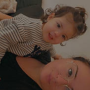 Ezelhya a rejoint le concours — aidez-le/la à gagner de superbes lots ! toddler, child, person, glasses, striped_shirt, curly_hair, smile, indoor, blanket, gift, couch, face, portrait, closeup, family, casual, warm, cozy, home, relaxed