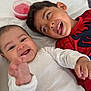 baby, child, infant, smiling, playful, bed, white_clothing, red_clothing, spiderman, tongue_out, hand, face, happy, sibling, indoors, candid, closeup, person, toddler, fun