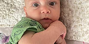 Stefan is registered to the contest to win money with this photo: baby, bed, blanket, butterfly_pattern, casual_clothing, child, close_up, comfortable, curious_expression, dinosaur_print, green_shirt, hand_near_face, indoors, infant, lying_down, pale_skin, portrait, soft_lighting, textured_blanket, wide_eyes