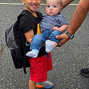 Noah joined the competition — help win amazing prizes! child, baby, boy, smiling, holding, backpack, tattoo, adult, jeans, shorts, socks, shoes, asphalt, outdoor, person, casual_clothing, striped_shirt, black_tshirt, red_shorts, family
