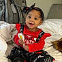 baby, child, smiling, red_clothing, black_clothing, headband, toy, bed, blanket, backpack, indoors, person, happy, sitting, footwear, black_shoes, cute, infant, playful, portrait