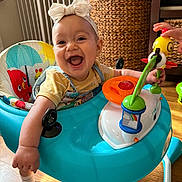 Milania is registered to the contest to win money with this photo: baby, bow, headband, walker, toy, smiling, happy, indoor, child, play, hand, floor, wicker, basket, colorful, clothing, person, furniture, wood, cute