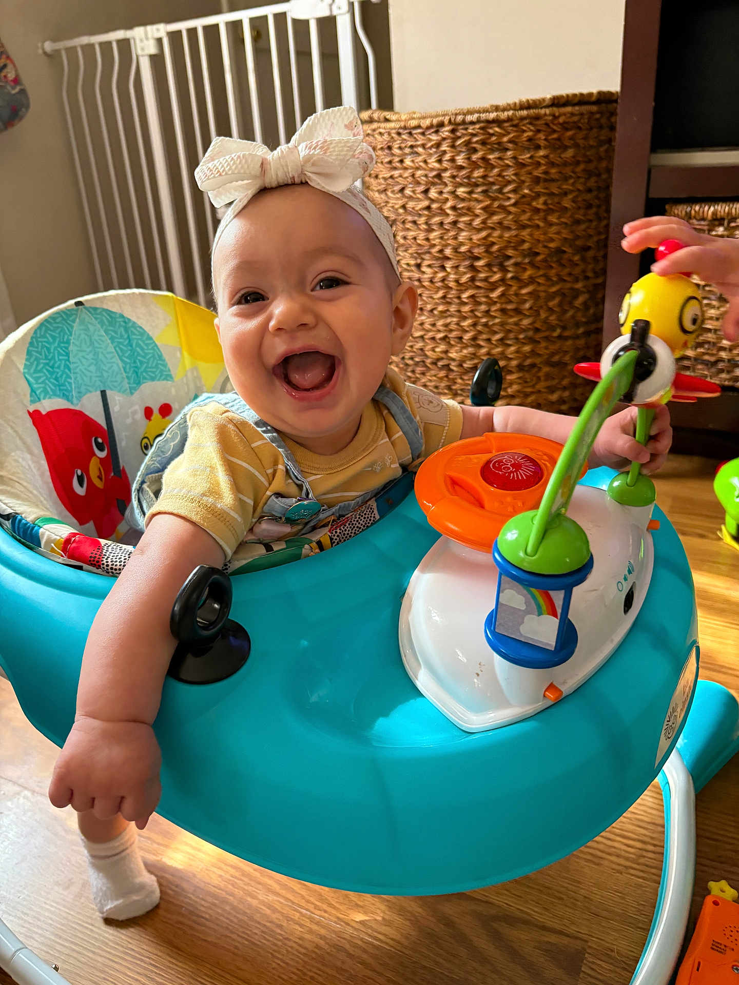 Milania is registered to the contest to win money with this photo: baby, bow, headband, walker, toy, smiling, happy, indoor, child, play, hand, floor, wicker, basket, colorful, clothing, person, furniture, wood, cute