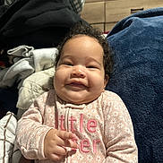 Zaylani joined the competition — help win amazing prizes! baby, smiling, curly_hair, pink_onesie, floral_pattern, hand, blanket, indoor, drawer, cozy, child, portrait, cute, infant, person, home, soft_texture, clothing, happy, young