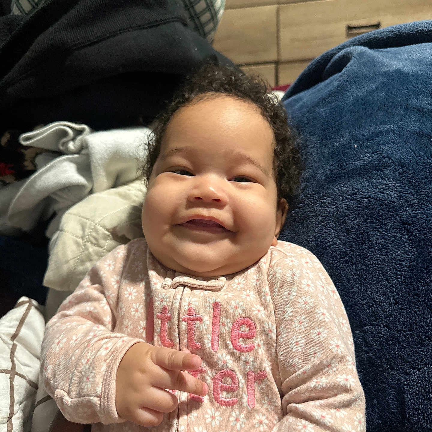 Zaylani joined the competition — help win amazing prizes! baby, smiling, curly_hair, pink_onesie, floral_pattern, hand, blanket, indoor, drawer, cozy, child, portrait, cute, infant, person, home, soft_texture, clothing, happy, young