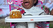 Azai is registered to the contest to win money with this photo: baby, birthday, cake, celebration, child, clothing, cute, event, face, food, footwear, fun, grass, happy, high_chair, outdoor, party_hat, person, sitting, smiling