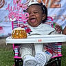 baby, birthday, cake, celebration, child, clothing, cute, event, face, food, footwear, fun, grass, happy, high_chair, outdoor, party_hat, person, sitting, smiling