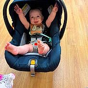 Jace is registered to the contest to win money with this photo: arms_up, baby, bib, bright, car_seat, child, clothing, cute, expression, foot, happy, indoors, infant, person, playful, safety, seatbelt, smile, wooden_floor, young_child