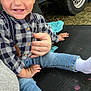 toddler, child, smiling, happy, jeans, checkered_shirt, socks, hand, outdoor, wheel, tire, fabric, person, sitting, casual, cute, clothing, skin, face, baby