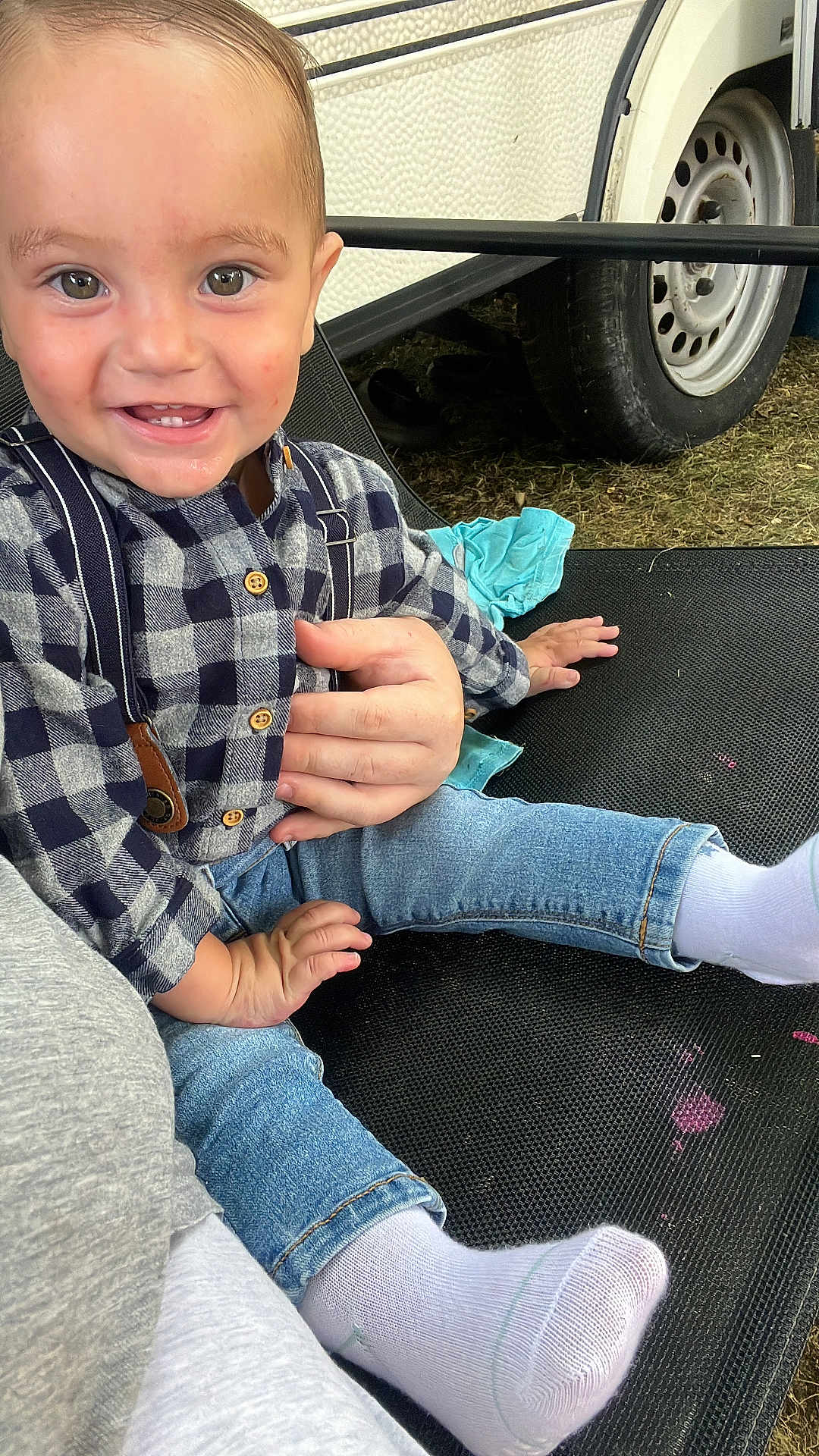 Eyden participe au concours pour gagner de l'argent avec cette photo : toddler, child, smiling, happy, jeans, checkered_shirt, socks, hand, outdoor, wheel, tire, fabric, person, sitting, casual, cute, clothing, skin, face, baby