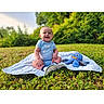 baby, blanket, blue_clothing, child, cute, daylight, grass, greenery, happy, infant, nature, octopus, outdoor, park, playtime, plush, sitting, smiling, sunlight, toy