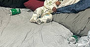 Dream is registered to the contest to win money with this photo: baby, child, pajamas, bed, pillow, striped_bed_sheet, soda_can, smile, indoor, sleepwear, messy_bed, person, headboard, fabric, cute, infant, relaxing, black_hair, lying_down, cozy