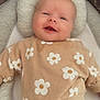 baby, smiling, sweater, flower_pattern, cushion, soft_toy, black_pants, infant, portrait, indoor, comfort, cute, child, cozy, apparel, headrest, happy, lying_down, closeup, casual_clothing
