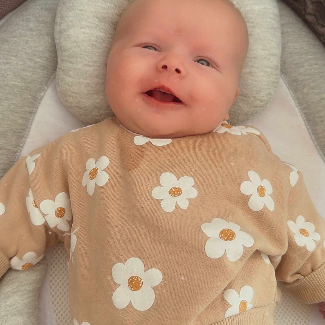 Ambre participe au concours pour gagner de l'argent avec cette photo : apparel, baby, black_pants, casual_clothing, child, closeup, comfort, cozy, cushion, cute, flower_pattern, happy, headrest, indoor, infant, lying_down, portrait, smiling, soft_toy, sweater