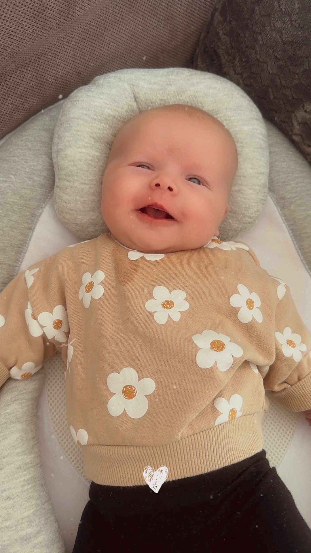 Ambre participe au concours pour gagner de l'argent avec cette photo : baby, smiling, sweater, flower_pattern, cushion, soft_toy, black_pants, infant, portrait, indoor, comfort, cute, child, cozy, apparel, headrest, happy, lying_down, closeup, casual_clothing