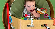 Jayden joined the competition — help win amazing prizes! baby, child, toy, play_area, green, cushion, carpet, infant, sitting, colorful, wooden, clothing, indoor, person, cute, looking_up, white_sock, playtime, floor, padded