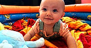 Mckenzie is registered to the contest to win money with this photo: baby, infant, playpen, blanket, toy, stuffed_animal, child, smiling, indoors, colorful, red, orange, blue, cute, happy, toddler, clothing, overalls, play, face