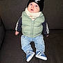Raphaël participe au concours pour gagner de l'argent avec cette photo : baby, child, infant, puffer_vest, beanie, hat, jeans, sneakers, couch, indoor, blue_eyes, clothing, footwear, person, seated, expression, curious, casual, warm_clothing, portrait