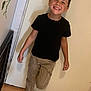 child, boy, smiling, black_tshirt, cargo_pants, indoor, door, floor_tiles, plant, happy, pose, footwear, sneakers, casual_clothing, young, playful, person, wall, standing, light
